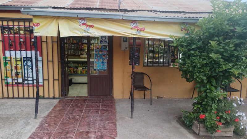 Frente de El Crillón con la puerta abierta, estanterías con abarrotes y golosinas, y una vitrina con productos detrás de la reja.